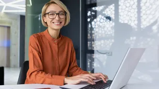 office worker sat at a laptop, smiling 