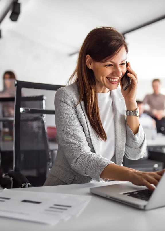 Woman in an office on phone and laptop with secure endpoint Security and Management solutions